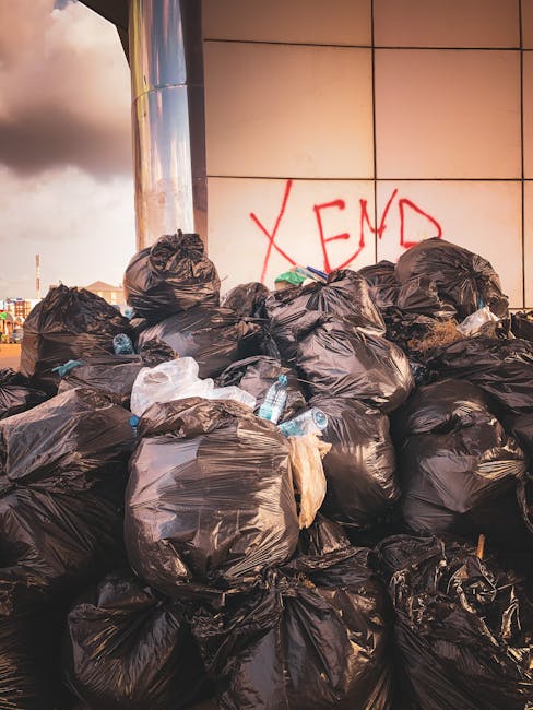 A section of ground covered with discarded packaging materials and rubbish, predominantly composed of flattened cardboard boxes with green and white branding, some torn and crumpled, scattered across