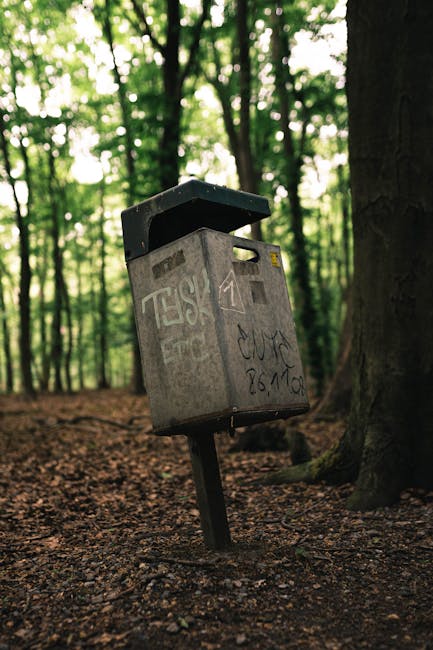 A cluttered outdoor scene showing multiple overflowing rubbish bins placed on a paved pavement in front of commercial premises. The largest bin is a grey mixed paper and card container, overflowing wi